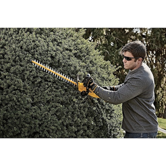 Lithium ion hedge trimmer being used by a person to mend hedge