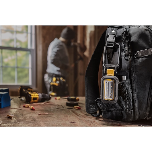 DEWALT task light attached to backpack using the hook feature while user works on something in the background 