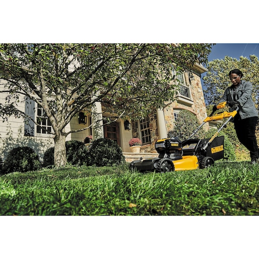 21 and a half inch Brushless Cordless Self Propelled mower in action by a person on the front lawn of a house