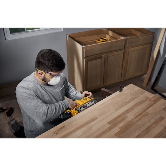 User sanding the side of a wooden kitchen cabinet with the DCW220B and the DCB250 battery 