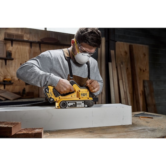 User sanding a wooden block with the DCW220B and DCBP520 battery attached