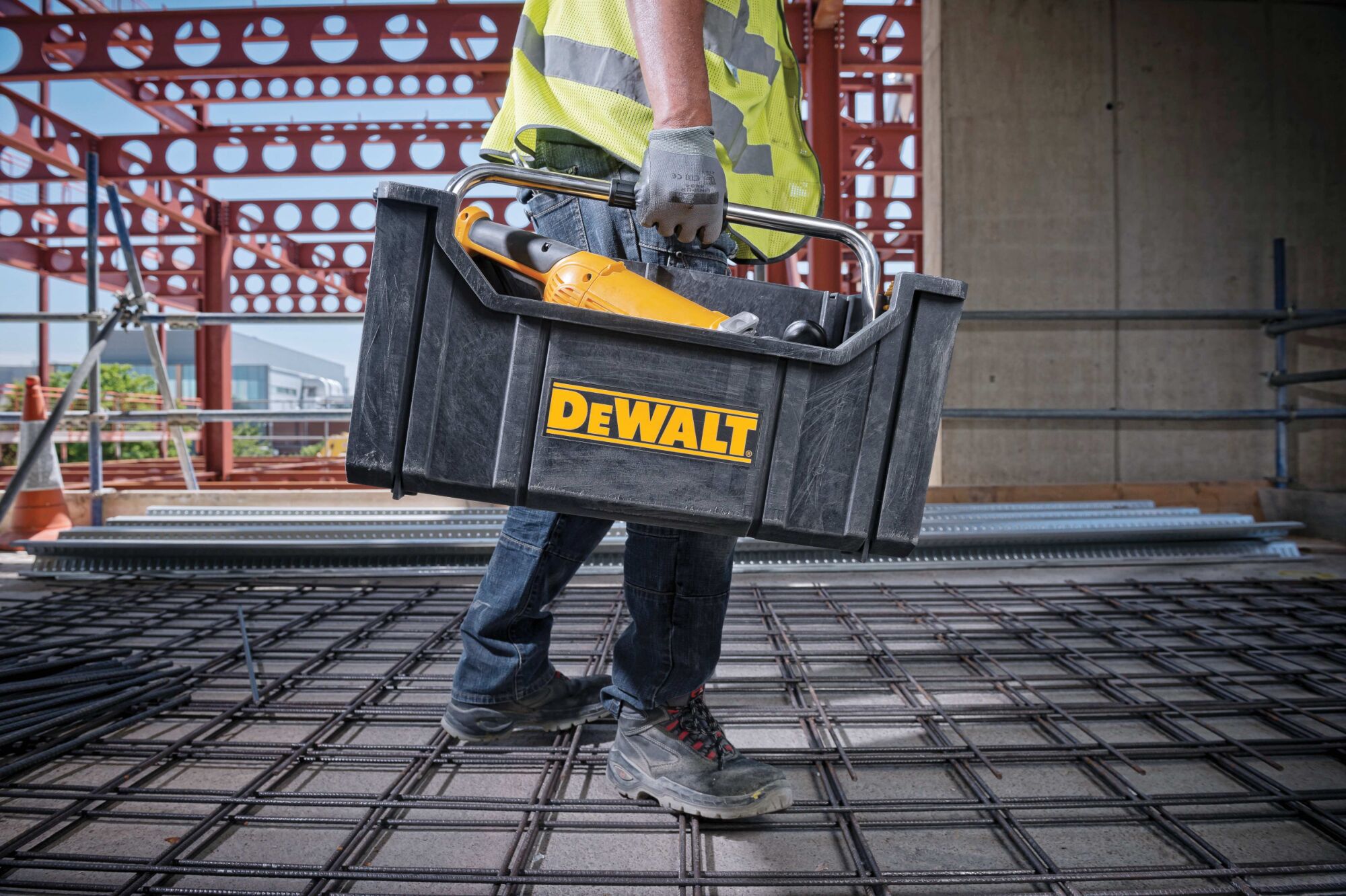 tough system tote with carrying handle filled with tools being carried by a worker at a worksite.