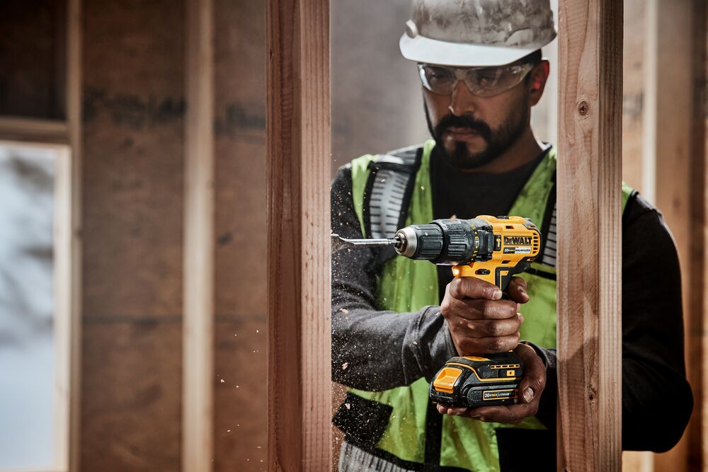 DEWALT Hammer Drill powered by a 20V 2Ah battery, used by a bare hands worker drilling a wooden structure.