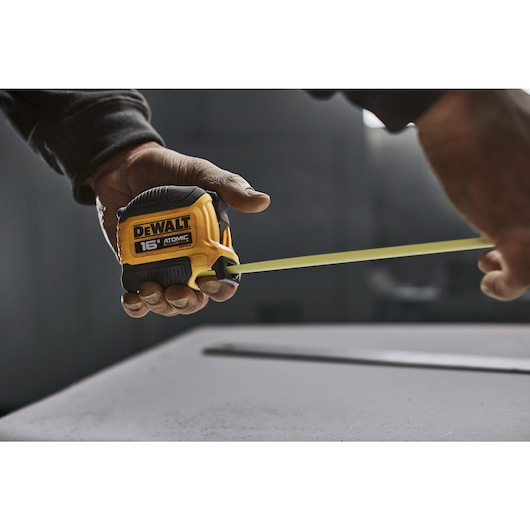 User holding finger brake while measuring drywall with DEWALT ATOMIC COMPACT SERIES Tape Measure.