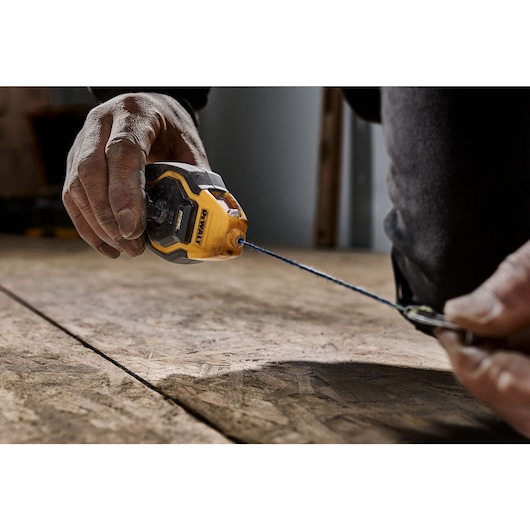 Person holding DEWALT ATOMIC COMPACT SERIES Chalk Reel for placement along plywood flooring.
