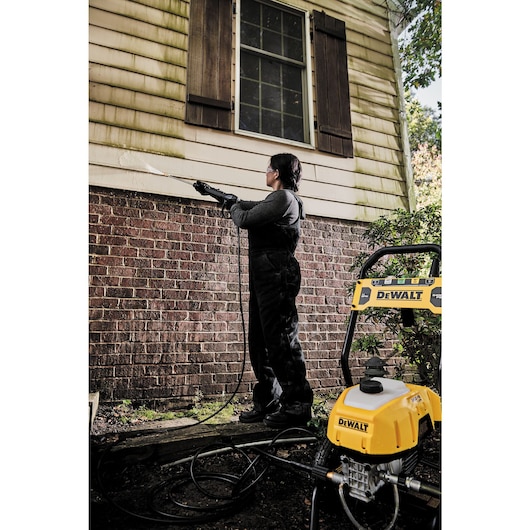 Electric cold water pressure washer being used to wash wall.