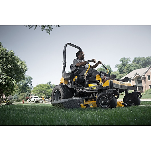 Backside view of 60 inch Kawasaki Gas Hydrostatic Commercial Zero Turn Mower being used by person to mow lawn.