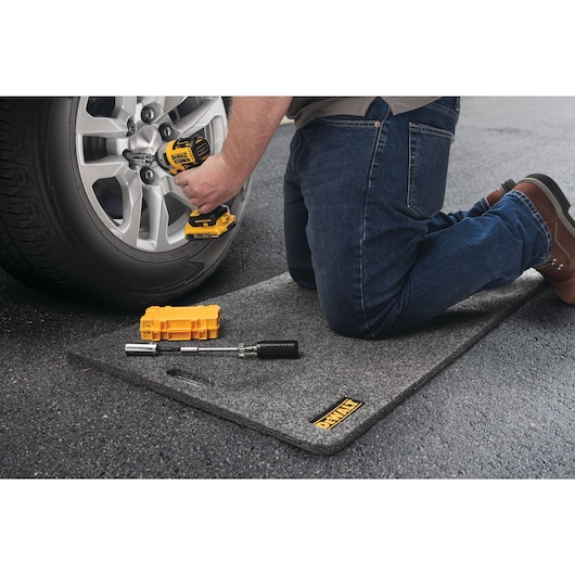 Utility Mat being used by a person while changing a tire of a car.